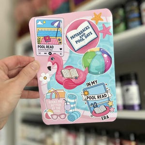 May include: A pink sticker with various summer-themed illustrations. It features a flamingo float, beach ball, and the text "POOL READ Summer Book Club." Other text includes "PAPERBACKS AND POOL DAYS" and "BOOKS ARE BETTER BY THE POOL."