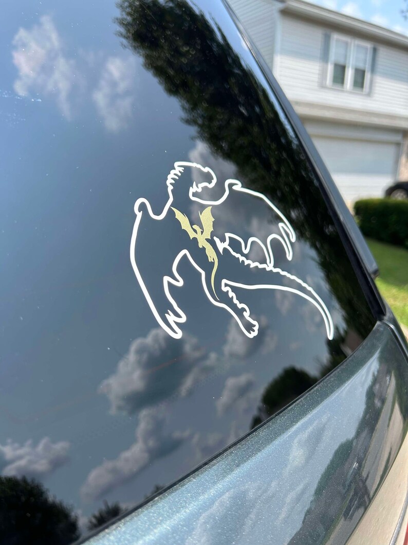 May include: A white silhouette of a dragon with a smaller dragon inside, on a black car window.