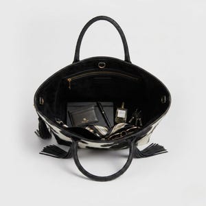 May include: Black and white cowhide patterned tote bag with black handles and tassels. The bag contains a wallet, pen, notebook, perfume, keys, and sunglasses. Internal measurements.