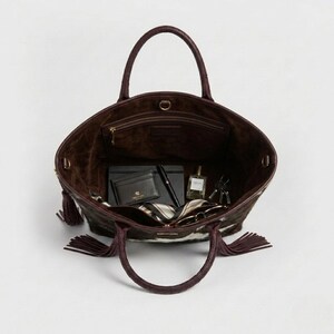 May include: A large open tote bag with a dark brown exterior and a lighter brown interior. The bag has a cowhide pattern with white and brown patches. Inside are a wallet, pen, notebook, perfume, keys, and a scarf.