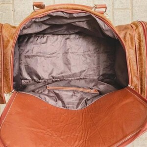 Puede incluir: Una bolsa de viaje de color marr&oacute;n claro con un compartimento principal grande y dos bolsillos laterales. El interior est&aacute; forrado con tela gris oscuro y cuenta con un bolsillo con cremallera. La bolsa tiene una abertura superior amplia.