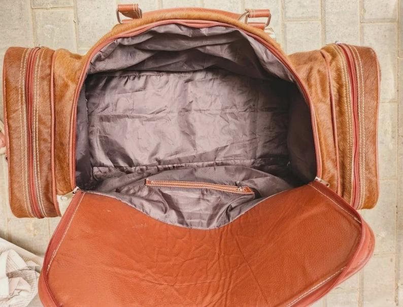 Puede incluir: Una bolsa de viaje de color marr&oacute;n claro con un compartimento principal grande y dos bolsillos laterales. El interior est&aacute; forrado con tela gris oscuro y cuenta con un bolsillo con cremallera. La bolsa tiene una abertura superior amplia.