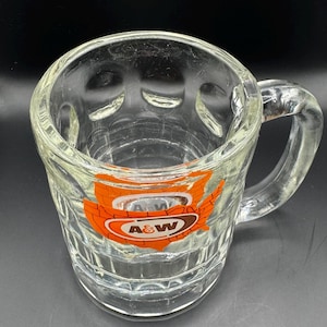 May include: A white ceramic mug with a black handle and the text "But First, Coffee" in a black, handwritten-style font. The mug is on a white surface.