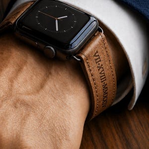 May include: A black smartwatch with a brown leather strap is shown. The strap is engraved with Roman numerals. The text "Engraved Just for Him" is at the top of the image.