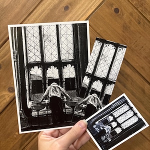 May include: A set of three black and white art prints featuring a figure standing before a large, multi-paned gothic window. The collection includes one rectangular print, one tall vertical bookmark-style print, and one small square print.