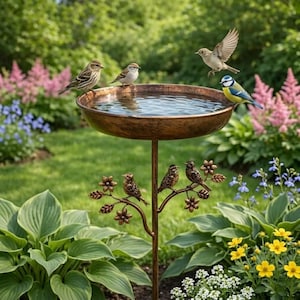 May include: A bronze bird bath with a shallow water-filled basin. Several small birds perch on the rim and a decorative branch below. The bird bath is set in a garden with green foliage and colourful flowers.