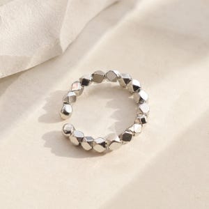 May include: A silver-toned open ring constructed from a series of small, faceted, geometric metallic beads linked together in a circular band. The ring features a gap at the front, showcasing a reflective, polished surface with multiple angles.