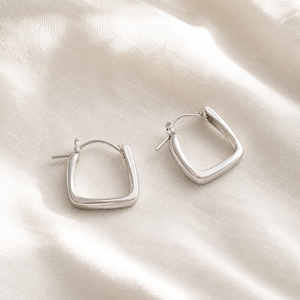 May include: A pair of silver-toned hoop earrings featuring a distinct square shape with rounded corners. Each earring has a smooth, polished metallic finish and a thin post closure mechanism, presenting a clean and simple geometric design.