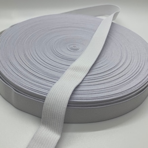 Puede incluir: Un rollo de cinta elástica blanca. La cinta elástica es plana y tiene una textura tejida. El rollo es circular, con la cinta enrollada firmemente en círculos concéntricos. El fondo es blanco liso.