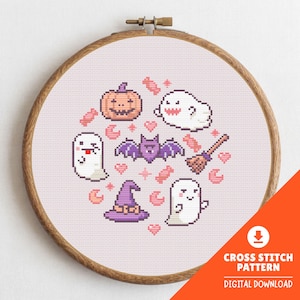 Puede incluir: Un bastidor de madera con un patrón de punto de cruz sobre tela rosa claro. El diseño presenta motivos pixelados de Halloween que incluyen una calabaza, tres fantasmas blancos, un murciélago morado, un sombrero de bruja, una escoba y dulces.