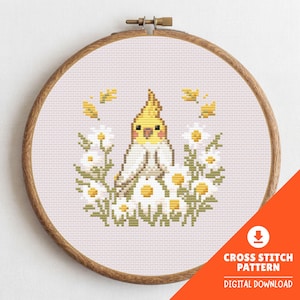 May include: A cross-stitch pattern featuring a yellow and white cockatiel surrounded by white daisies and yellow accents. The design is set within a wooden embroidery hoop. Text on the image reads "CROSS STITCH PATTERN DIGITAL DOWNLOAD".