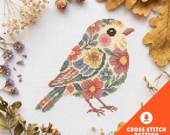 May include: A cross stitch pattern featuring a bird filled with a floral motif in shades of pink, yellow, blue, and green. The bird has a dark eye and is stitched on white fabric. The design is surrounded by dried flowers and oak leaves.