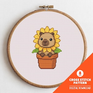 Puede incluir: Patrón de punto de cruz que muestra un carpincho en un girasol, en una maceta de terracota, dentro de un bastidor de bordado de madera. La imagen incluye el texto "CROSS STITCH PATTERN DIGITAL DOWNLOAD".