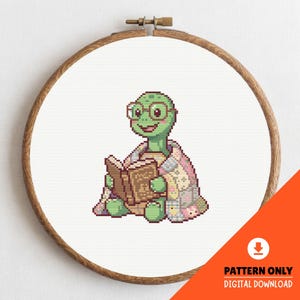 Puede incluir: Patrón de punto de cruz de una tortuga verde con gafas, leyendo un libro y envuelta en una colcha de retazos. El diseño está en un bastidor de bordado de madera. El texto en la imagen dice "PATTERN ONLY DIGITAL DOWNLOAD".