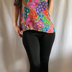 May include: A short-sleeved top with a patchwork design in vibrant colors like pink, green, purple, and red. The top is paired with black leggings. The overall style is casual and colorful.