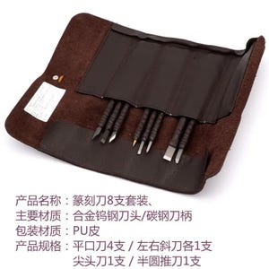 May include: A set of eight carving tools with dark handles and metal tips, organized in a brown faux leather roll-up case. The set includes four flat chisels, two angled chisels, one pointed tool, and one gouge, all secured within individual slots.