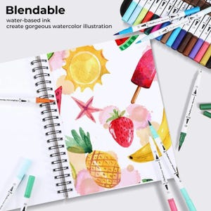 Op de afbeelding: Een spiraalgebonden schetsboek met aquarelillustraties van een gele zon, een rood waterijsje, een roze zeester, een rode aardbei en een gele banaan. Verschillende Ohuhu-markers met dubbele punt liggen rondom het notitieboek.