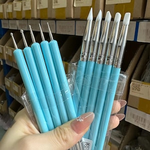 May include: A set of ten sculpting tools with light blue handles, featuring five metal ball-end styluses and five silicone-tipped brushes with various shapes, all encased in a clear plastic sleeve for organized storage and precision crafting.
