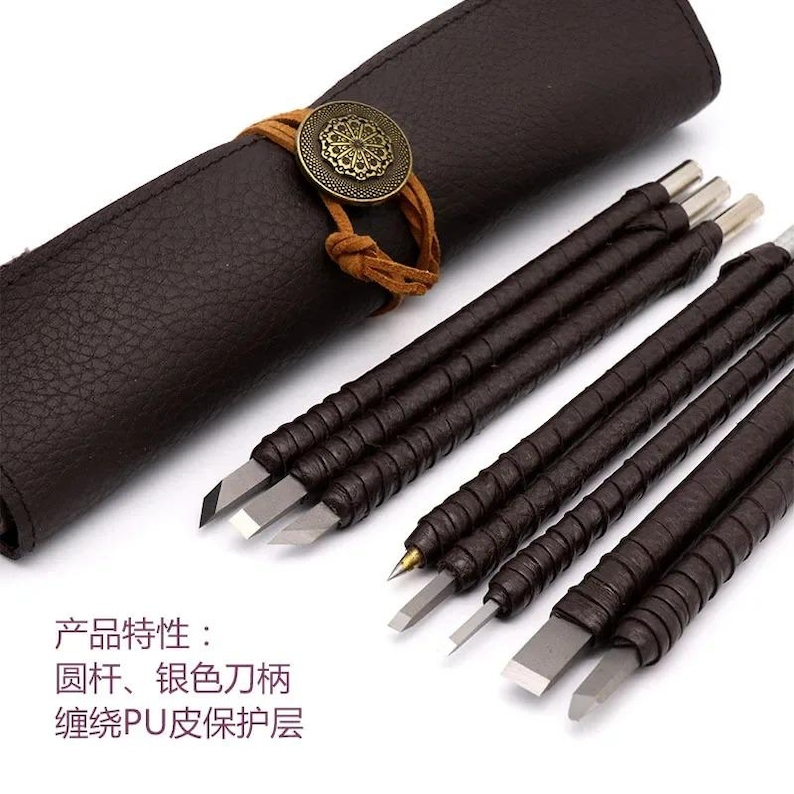 May include: A set of carving tools with silver metal blades and brown leather-wrapped handles, accompanied by a dark brown leather roll case secured with a tan cord and a circular brass-toned decorative button. Text reads: 产品特性：圆杆、银色刀柄、缠绕PU皮保护层.