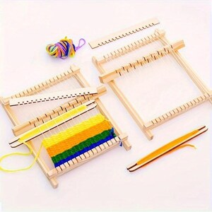May include: A set of wooden weaving looms with colorful yarn. The looms are rectangular with white threads stretched across. One loom has a partially woven piece with yellow, green, and blue yarn. A wooden shuttle and a ball of multi-colored yarn are also present.