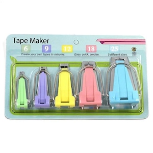Peut inclure: Un ensemble de cinq appareils à biais dans un emballage blister en plastique. Les outils sont de couleur vert clair, violet, jaune, rose et bleu, et sont étiquetés avec les tailles 6, 9, 12, 18 et 25. L'emballage porte le texte Tape Maker, Create your own tapes in minutes, Easy, quick, precise, et 5 different sizes.
