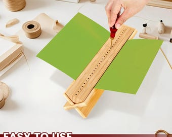 May include: A light-colored bamboo bookbinding cradle with a V-shaped base and a central row of evenly spaced holes. A red-handled awl is inserted into one of the holes, piercing a sheet of bright green paper held within the wooden structure.