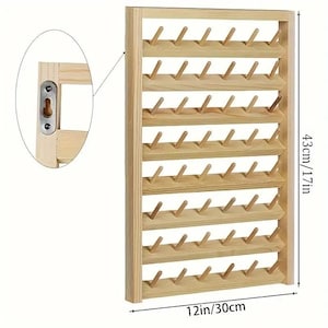 Peut inclure: Un support mural en bois clair pour bobines de fil, doté de huit rangées horizontales de tiges. Le support mesure 30 cm de large sur 43 cm de haut. Un encart circulaire montre une plaque de fixation métallique en trou de serrure sur le cadre.