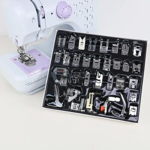 Peut inclure: Une machine à coudre blanche et violet clair placée derrière un plateau en plastique noir contenant un ensemble complet de trente-deux pieds-de-biche assortis en métal et en plastique, organisés dans des compartiments moulés individuels.