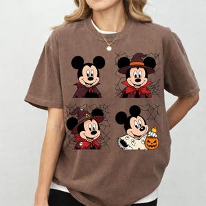 May include: A brown short-sleeve t-shirt featuring four square panels of Mickey Mouse in various Halloween costumes, including a vampire cape, a witch hat, and a ghost-patterned outfit, with spider web graphics in the background.