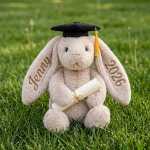 May include: A beige plush rabbit with long ears, wearing a black graduation cap with a yellow tassel. The left ear is embroidered with the name Jenny in brown thread, and the right ear features the year 2026. The rabbit holds a rolled diploma.