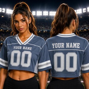 May include: A slate blue cropped jersey featuring a V-neckline with white and grey stripes. The front and back display the text "YOUR NAME" in white block letters above the number "00" in a matching white font with a grey outline.