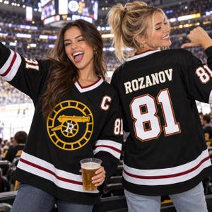 May include: A black hockey jersey featuring a yellow circular logo with a cannon and the letter R in the center. The jersey has white and maroon stripes on the sleeves and hem, the number 81, the name ROZANOV, and a captain C patch.