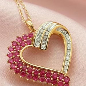 May include: A gold heart-shaped pendant necklace featuring a cluster of round, vibrant pink rubies along the left side and a channel of small, sparkling white diamonds set into a polished gold and silver-toned metal band on the right side.