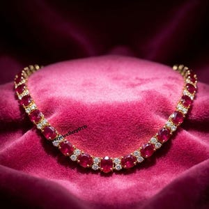 Könnte beinhalten: Eine goldfarbene Halskette mit einer durchgehenden Reihe oval geschliffener, tiefroter Rubine, die sich mit kleinen, klaren, rund geschliffenen weißen Steinen abwechseln. Das Schmuckstück ist halbkreisförmig angeordnet und zeigt ein wiederkehrendes Muster.