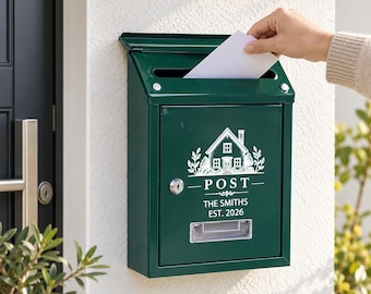 Peut inclure: Une boîte aux lettres murale en métal vert foncé avec un motif blanc représentant une maison, le mot POST et le texte THE SMITHS EST. 2026. Elle possède une fente supérieure, une serrure centrale et une petite fenêtre transparente en bas.