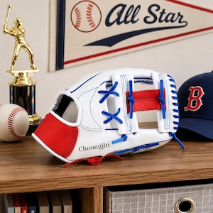Puede incluir: Un guante de béisbol blanco con detalles en rojo y azul, con cordones azules y el nombre Choongjin impreso en negro en el lateral. El guante está construido con una sección de palma roja y correas de cuero azul en la zona de la red.