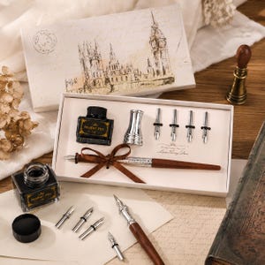 Peut inclure: Un ensemble de calligraphie comprenant un stylo en bois avec un ruban marron, un encrier en verre &eacute;tiquet&eacute; The Feather Pen, un porte-plume argent&eacute; et cinq plumes m&eacute;talliques interchangeables. Le tout est pr&eacute;sent&eacute; dans une bo&icirc;te blanche illustr&eacute;e.