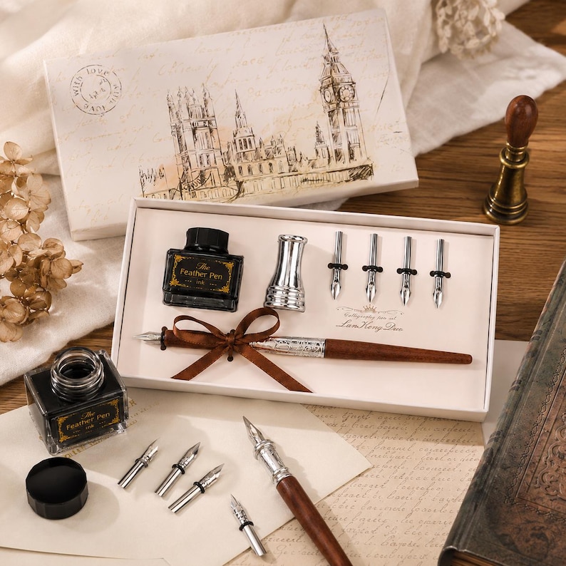 Peut inclure: Un ensemble de calligraphie comprenant un stylo en bois avec un ruban marron, un encrier en verre &eacute;tiquet&eacute; The Feather Pen, un porte-plume argent&eacute; et cinq plumes m&eacute;talliques interchangeables. Le tout est pr&eacute;sent&eacute; dans une bo&icirc;te blanche illustr&eacute;e.