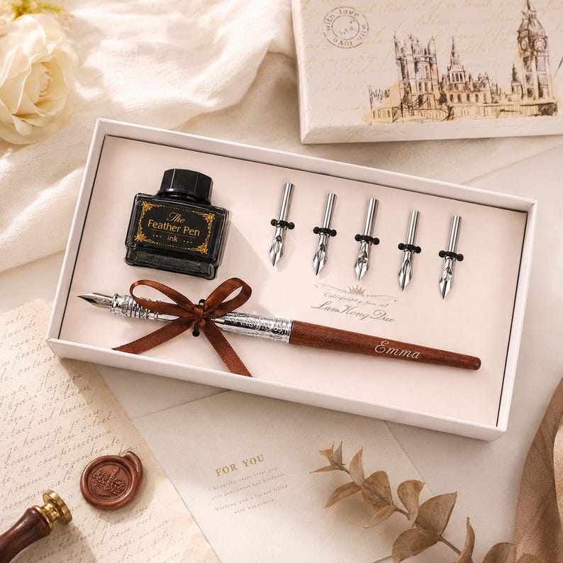 Peut inclure: Un ensemble de calligraphie dans une bo&icirc;te blanche comprenant un stylo en bois avec un ruban marron, un flacon d'encre noire &eacute;tiquet&eacute; The Feather Pen et cinq plumes en m&eacute;tal argent&eacute;. Le stylo est grav&eacute; du pr&eacute;nom Emma. Le couvercle montre Big Ben.