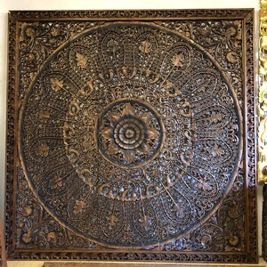 Puede incluir: Panel de madera tallada cuadrada y grande, con intrincados detalles. El panel marr&oacute;n oscuro presenta un dise&ntilde;o floral central rodeado de patrones detallados y arremolinados y un borde decorativo. El tallado es muy detallado y crea una superficie texturizada.