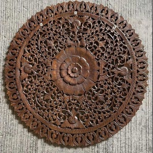 Può includere: Un grande pannello da parete circolare in legno marrone scuro con intricati motivi floreali e vegetali intagliati a mano. Il design è centrato su un fiore in piena fioritura, circondato da un fitto fogliame e da un bordo smerlato. Le etichette 1, 2 e 3 sono visibili.