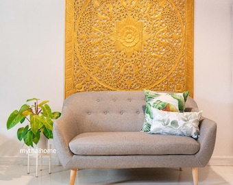 Könnte beinhalten: Ein graues Stoff-Sofa mit Knöpfen und Holzbeinen vor einer großen, kunstvoll geschnitzten Holz-Wandverkleidung in Gold. Das Sofa hat zwei Kissen mit tropischem Blatt-Muster.