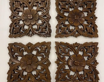 May include: Four intricately carved wooden wall plaques with a floral design. Each plaque features a central flower surrounded by intricate leaf patterns. The plaques are made of dark brown wood and have a rustic, antique look.