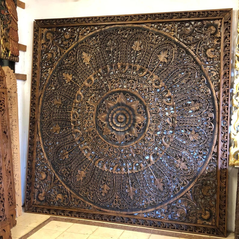 Puede incluir: Gran panel de pared de madera tallada con un dise&ntilde;o floral central y patrones ornamentados. El panel es de color marr&oacute;n intenso con acentos m&aacute;s oscuros, creando un efecto tridimensional. El panel cuadrado est&aacute; enmarcado con un borde detallado.