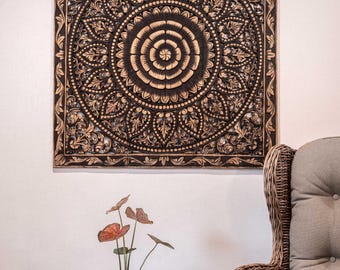 Könnte beinhalten: Ein quadratisches Wandpaneel aus Holz mit aufwendigen, handgeschnitzten Blumen- und Mandala-Mustern. Das Design besteht aus einem zentralen kreisförmigen Motiv, das von symmetrischen Blatt- und Blüten-Schnitzereien umgeben ist, in einem dunklen Holzton.