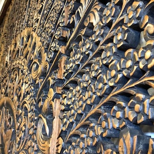 Puede incluir: Primer plano de un panel de madera tallada con un dise&ntilde;o floral y de hojas. La madera est&aacute; te&ntilde;ida de color marr&oacute;n oscuro, con reflejos marr&oacute;n claro. Las intrincadas tallas crean un efecto texturizado y tridimensional.