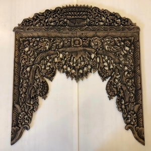 May include: A large, intricately carved wooden wall decor piece in a dark brown colour. The piece is shaped like an archway with floral designs and intricate details.
