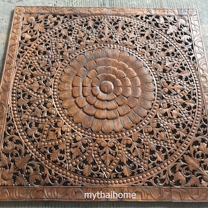 Puede incluir: Un gran panel de pared de madera tallada intrincadamente con un diseño circular en el centro. El panel está hecho de madera marrón oscura y presenta un patrón floral con un centro elevado.