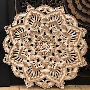 May include: White wooden wall decor with a carved mandala design in a brown color. The mandala has a circular shape with intricate details and a floral pattern.