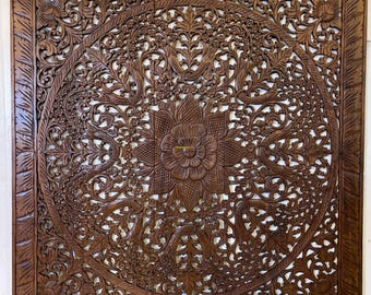 Könnte beinhalten: Eine große, aufwendig geschnitzte Holz-Wandverkleidung mit einem floralen Design. Die Verkleidung ist aus dunkelbraunem Holz und hat eine quadratische Form. Das Design zeigt eine große zentrale Blume, die von kleineren Blumen und Blättern umgeben ist. Die Verkleidung ist perfekt, um jedem Raum einen Hauch von Eleganz und Raffinesse zu verleihen.
